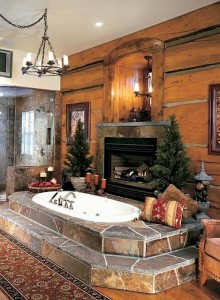 Stones surround the oval tub with a vie3w of the store fireplace and wood plank walls.